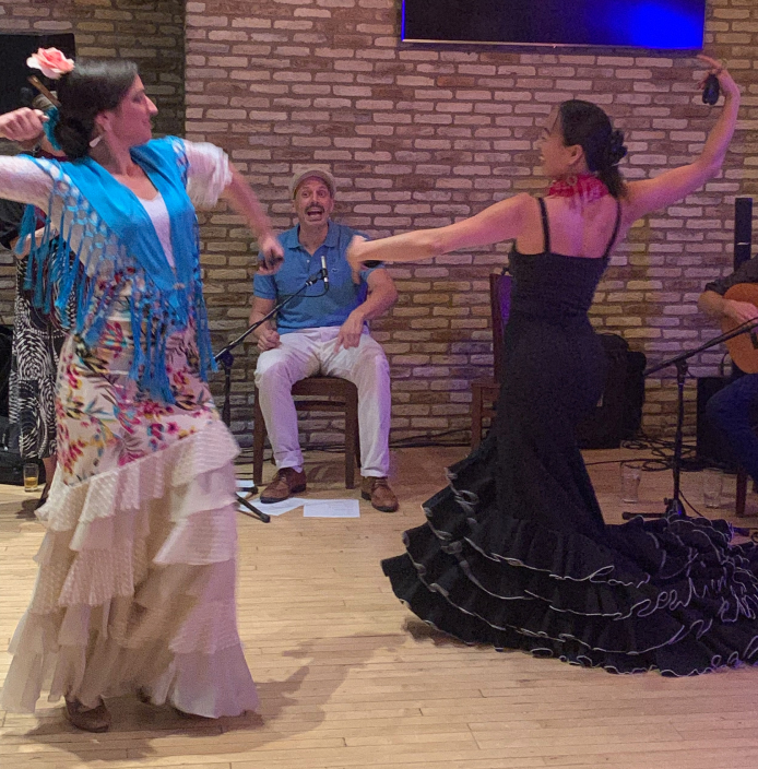 Two flamenco dancers performing at MetroNOME Brewery, one in a floral dress and another in black, accompanied by live musicians.